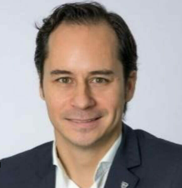 Impact Fellowship | curaJOY A man in a suit is smiling for the camera during a healthcare equity conference.