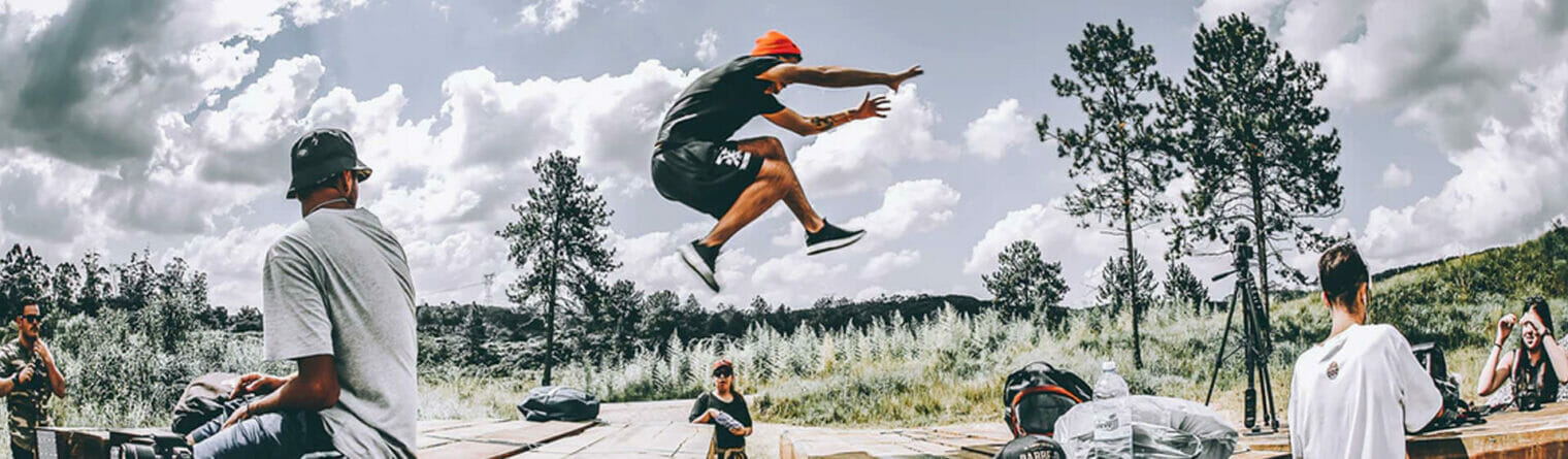 A man in a red shirt is doing a trick on a skateboard.