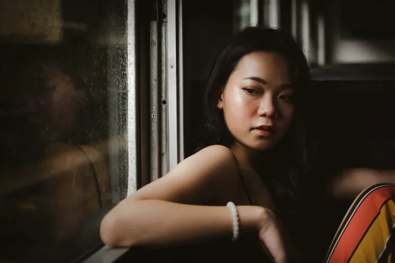 A woman with long dark hair sits by a window on a bus, looking outside with a thoughtful expression. Rain is visible on the window, evoking themes of behavioral health and self-reflection championed by curaJOY.