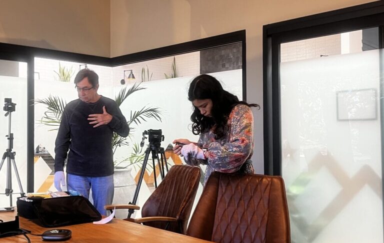Two people stand beside a conference table with electronic equipment; cameras and tripods are set up around the modern meeting room, highlighting an environment ideal for youth engagement or a youth ambassador internship.