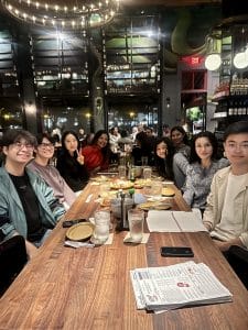 A group of people sit around a wooden table in a restaurant, with menus, drinks, and food items in front of them. The cozy, dimly lit space fosters family wellness as they connect under the decorative lights overhead.