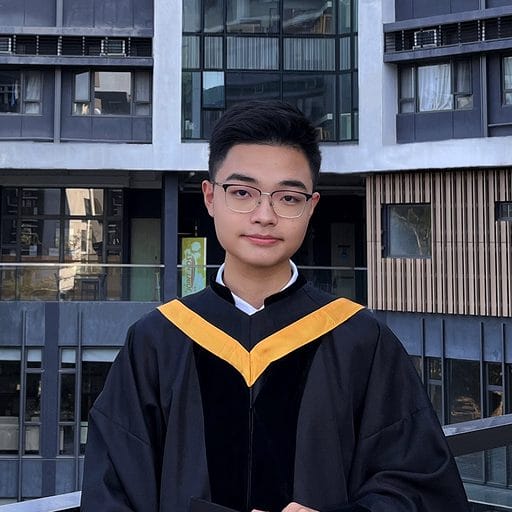 Safe to Break, Ready to Ship | curaJOY A person wearing glasses and a black and yellow graduation gown stands outside a building with large windows.