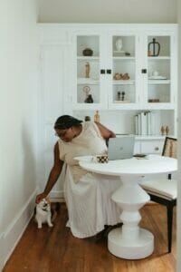 A woman sitting at a white table with a cat, emphasizing the importance of parenting for behavioral therapy.